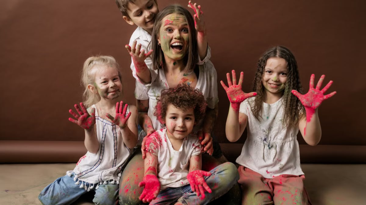 A happy group of children and woman covered in colorful powder, all smiles and joy.